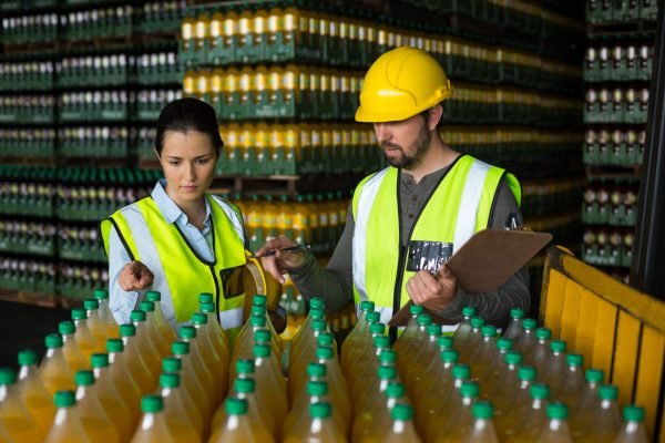 Two factory workers monitoring cold drink bottles at drinks production factory